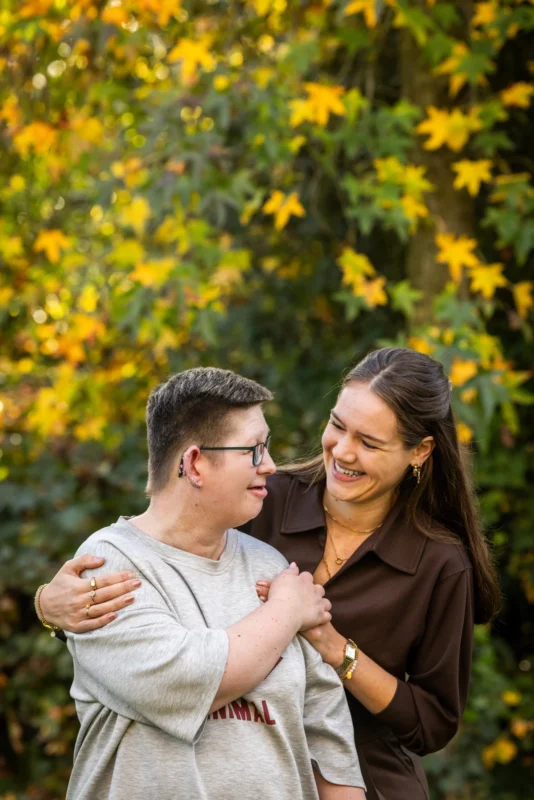 Cliënt en vrijwilliger kijken naar elkaar. Ze staan buiten in het groen, omringt met gele bloemetjes.