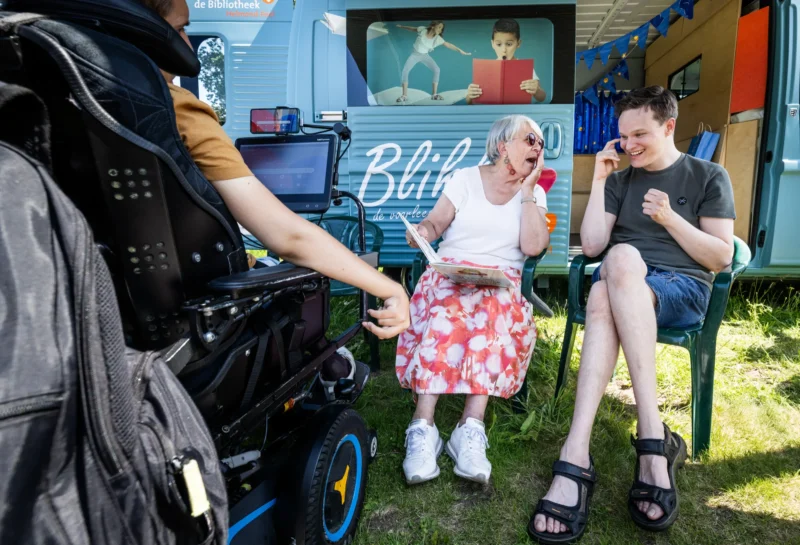 Voorleesbus Blikkie. Mevrouw leest cliënten voor uit een mooi boek.